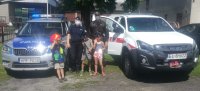 dzieci z policjantką i strażakiem obok samochodów