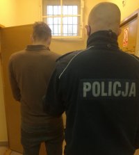 zatrzymany mężczyzna oraz umundurowany policjant stojący tyłem w pomieszczeniu dla osób zatrzymanych