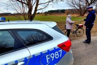 Policjant umundurowany wręcza odblask starszej pani jadącej na rowerze.
