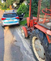 Wiejska droga, radiowóz policyjny stoi przed czerwonym traktorem.