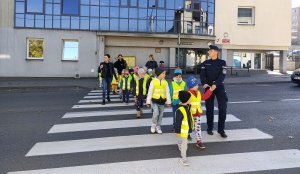 Dzieci wspólnie z policjantką przechodzą przez przejście dla pieszych.