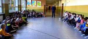 Dzieci siedzące na korytarzu szkoły i policjant.
