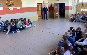 Dzieci siedzące na podłodze w klasie i policjant w mundurze.