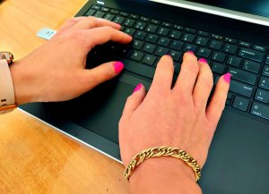 dłonie kobiety , paznokcie pomalowane, trzymane na klawiaturze laptopa, na prawej ręce bransoletka, na lewej zegarek