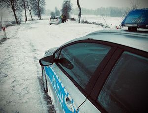 Radiowóz policyjny, droga zaśnieżona inne auto w zaspach i policjant.