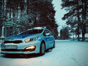 Radiowóz policyjny stojący na drodze w tle zaśnieżony las.