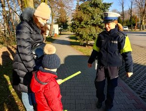 Policjantka wręczająca odblask dziecku idącemu z mamą.