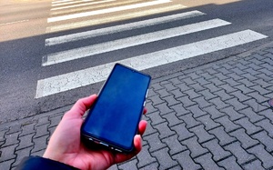Telefon komórkowy trzymane w ręce i w tle przejście dla pieszych.