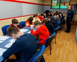 Dzieci siedzące przy stole piszące test wiedzy i policjantka.