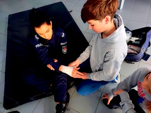 Chłopiec bandażujący rękę policjantce.