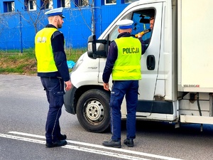 Policjanci w mundurach i kamizelkach odblaskowych podczas wykonywania badania trzeźwości kierującego busem.