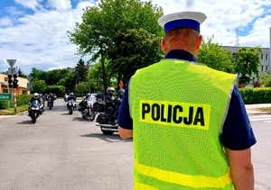 Policjant w mundurze stojący na skrzyżowaniu zabezpieczający przejazd motocykli.