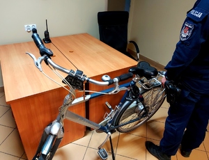 Rower stojący w pomieszczeniu obok policjant w mundurze.
