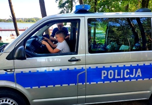 Chłopiec siedzący za kierownicą radiowozu i policjant.