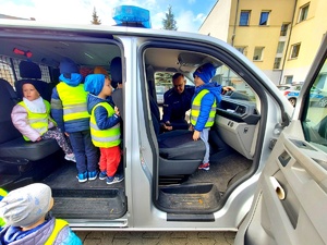 Dzieci w radiowozie i policjant pokazuje jak włącza się sygnały świetlne.
