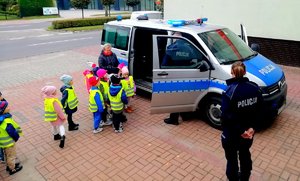 Dzieci i radiowóz policjantka stojąca tyłem w mundurze.