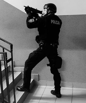 Policjant z długa bronią mierzy w kierunku schodów.