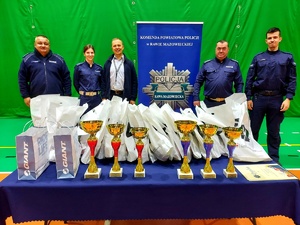 policjanci w mundurach obok gwiazdy policyjnej oraz pracownik WORD Skierniewice przy stole pełnym nagród i pucharów.