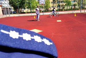 pagon policjanta i chłopiec jadący na rowerze obok pachołki i mężczyzna.
