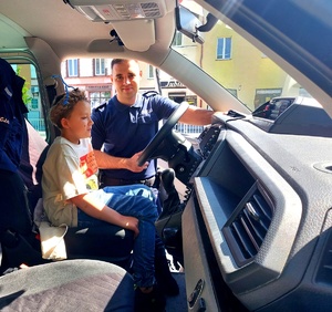 policjant i chłopiec siedzący w radiowozie za kierownicą.