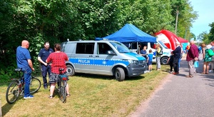 radiowóz i  policjant rozmawiający z osobami na rowerach.