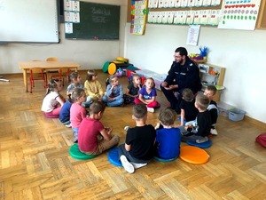 policjant siedzący na małym krzesełku u w kółku siedzą dzieci.