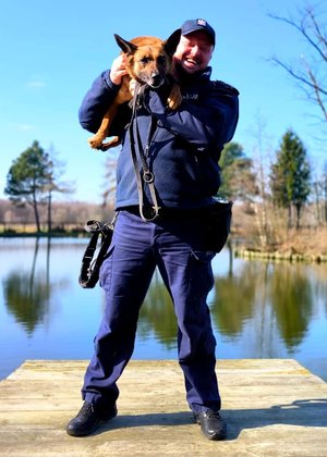 Policjant trzymający psa na ramieniu w tle jezioro.