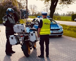 Policjant stojący przy motorze, motocyklista i radiowóz.