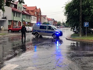 Radiowóz stojący w poprzek drogi i policjant kierujący ruchem w deszczu.