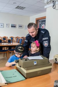 policjant i dwoje dzieci chłopczyk i dziewczynka ,pokazuje im stary sprzęt policyjny