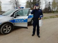 Umundurowany Policjant obok radiowozu z maskotką oraz torebka z prezentem.