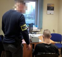 Nieumundurowany policjant stojący obok siedzącego mężczyzny.