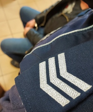 Pagon policjanta i ręce w kajdankach zatrzymanego mężczyzny.