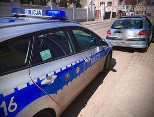 Radiowóz oznakowany i niebieski samochód osobowy.
