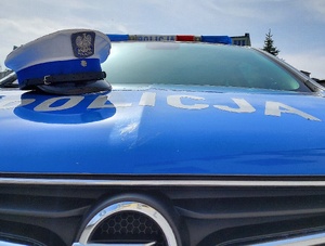 Maska radiowozu oznakowanego, niebieska z napisem policja i czapka policyjna z białym otokiem.