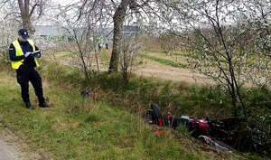 Policjant w mundurze i kamizelce odblaskowej a w rowie leży rozbity czerwony motor.