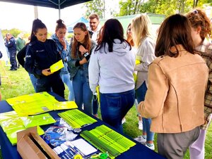 Policjantka rozdaje kamizelki i odblaski uczniom na stoisku policyjnym.