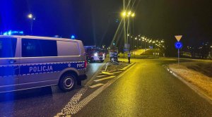 Radiowóz policyjny stojący bokiem, przewrócona latarnia i znaki drogowe.