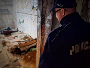 Policjant w mundurze wewnątrz budynku gdzie leżą porozrzucane ubrania.