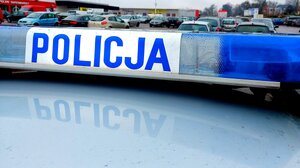 Napis policja na radiowozie w tle samochodów na parkingu.