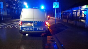 Radiowóz policyjny z włączonymi sygnałami świetlnymi stojący przy przejściu dla pieszych.