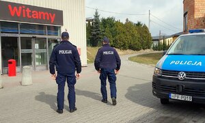 Policjanci idący w stronę marketu obok radiowóz.