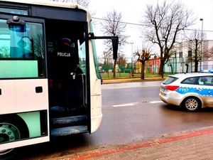 Policjant w mundurze kontroluje autokar obok stoi radiowóz.