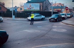 Policjant na skrzyżowaniu kieruje ruchem oraz samochody.