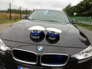 Radiowóz policyjny nieoznakowany i dwie czapki policyjne leżące na masce.