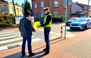 Policjant wręcza kamizelkę odblaskową pieszemu.