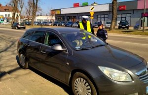 Policjant i policjantka stoją przy aucie w którym siedzi kierująca i rozmawiają.