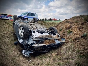 Samochód leżący na dachu w rowie, na drodze stoi radiowóz.