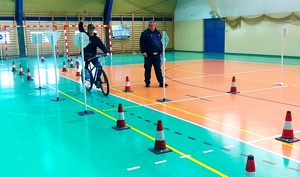 Chłopiec jadący na rowerze pomiędzy znakami drogowymi z ręką podniesioną do góry obok policjant w mundurze.