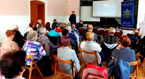 Policjant stojący przed widzami i prowadzi prelekcje na temat zakupów w sieci.